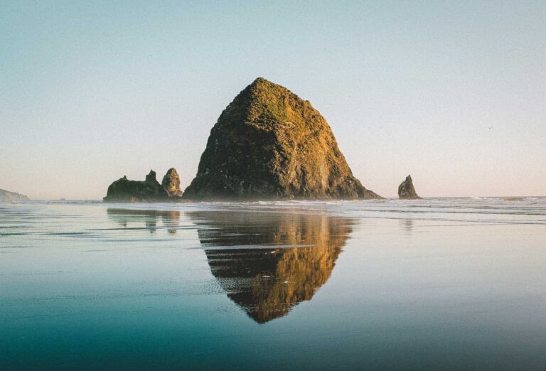 Cannon Beach in summer with Haystack Rock reflecting in the ocean's water.