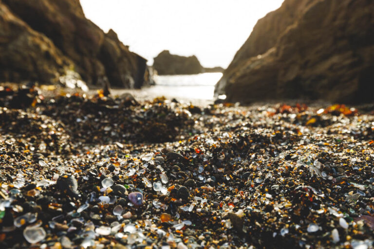 A low camera angle shot at Glass Beach with glass pebbles below and the rocky ocean in the distance.