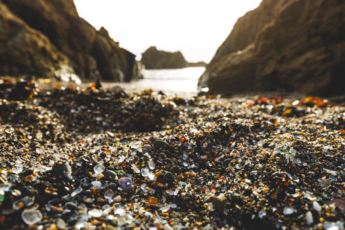 A low camera angle shot at Glass Beach with glass pebbles below and the rocky ocean in the distance.
