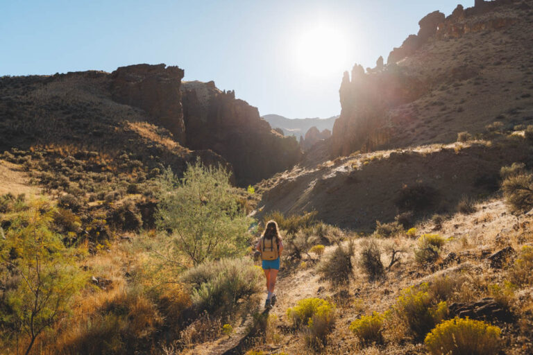A sunburst in the sky as Nina walks along a trail with beautiful rocks and cliffs in the distance.
