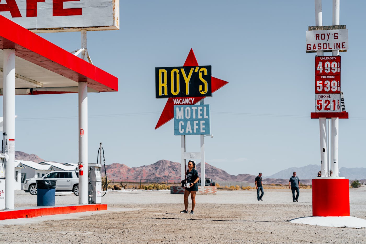 A bright gas station and motel with a desert backdrop, featuring people and vibrant signage.