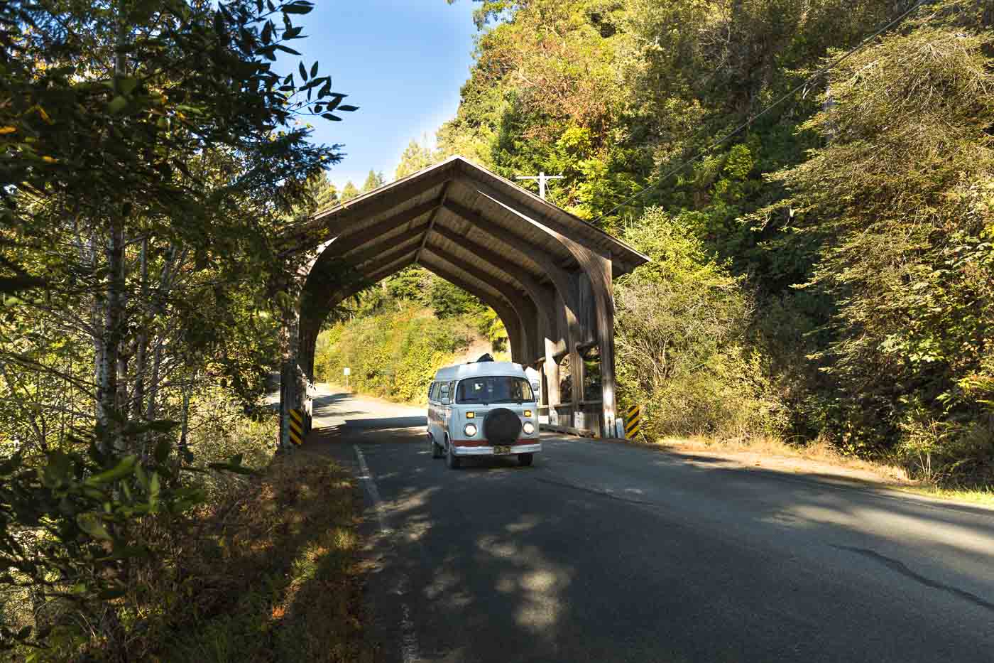 A VW Bus driving through a small covered bridge on Howland Hill Road in Jedediah Smith Redwoods State Park, California
